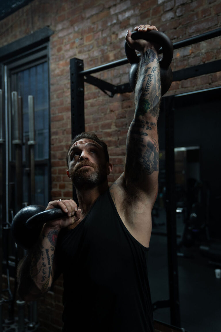 Dave Cash pressing a kettlebell overhead in front of a brick wall