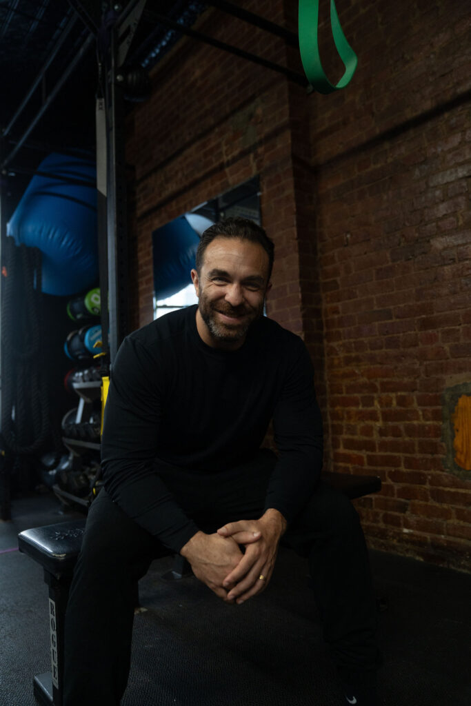 Dave Cash seated on a gym bench with his hands clasped, smiling